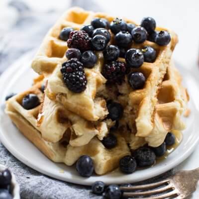 Stack of Belgian waffles on white background with berries and fork