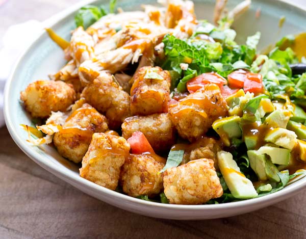 Comfort food meets salad greens. Get obsessed over this salad combo... crispy take-me-back-to-my-childhood tater tots, warm grilled chicken and crunchy shredded greens all smothered in BBQ sauce for the win!