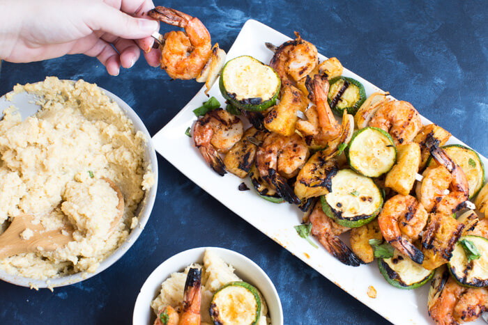 A classic southern dish gets a smoky twist with these Smoky Cheddar Cauliflower Grits and Cajun Shrimp. Cheesy cauliflower grits are served alongside sweet and spicy shrimp skewers with zucchini and pineapple.