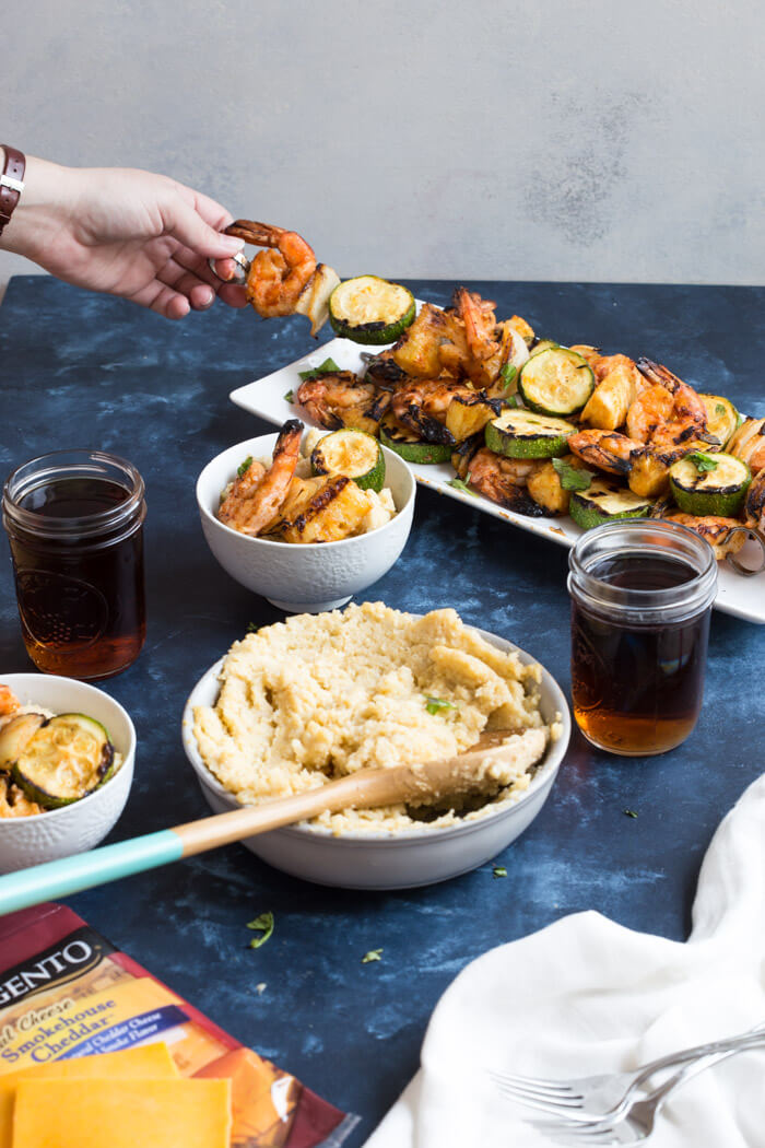 A classic southern dish gets a smoky twist with these Smoky Cheddar Cauliflower Grits and Cajun Shrimp. Cheesy cauliflower grits are served alongside sweet and spicy shrimp skewers with zucchini and pineapple.