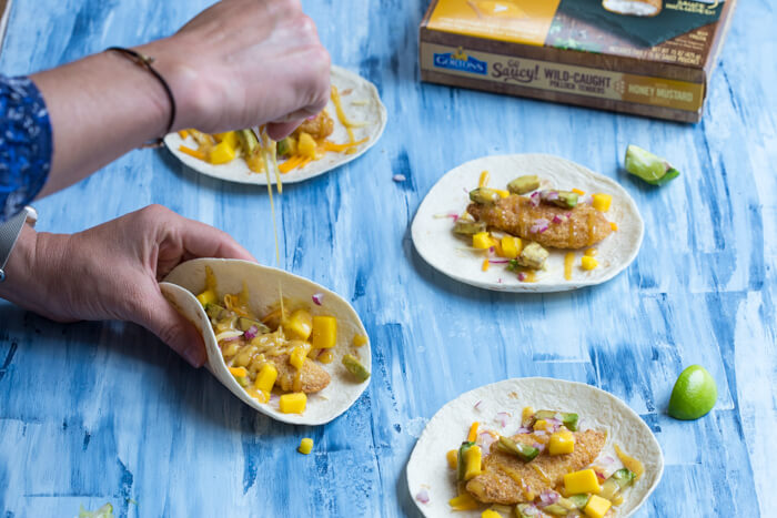 Honey Mustard Fish Tacos made with wild caught pollock tenders, onion, mango, avocado, and cheese nestled in a tortilla and drizzled with honey mustard! A tasty dinner on the table in less than 20 minutes.