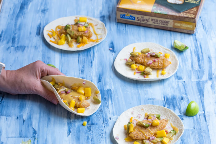 Honey Mustard Fish Tacos made with wild caught pollock tenders, onion, mango, avocado, and cheese nestled in a tortilla and drizzled with honey mustard! A tasty dinner on the table in less than 20 minutes.