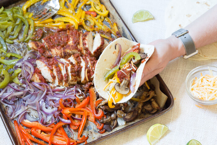 Sheet Pan Chicken Fajitas are our new weeknight dinner wonder. Check it, all the fajita veg plus super moist flavor packed chicken loaded on one pan and baked in the oven... then wrapped in soft tortillas and topped with cheddar, sour cream and avocado. What's not to love?