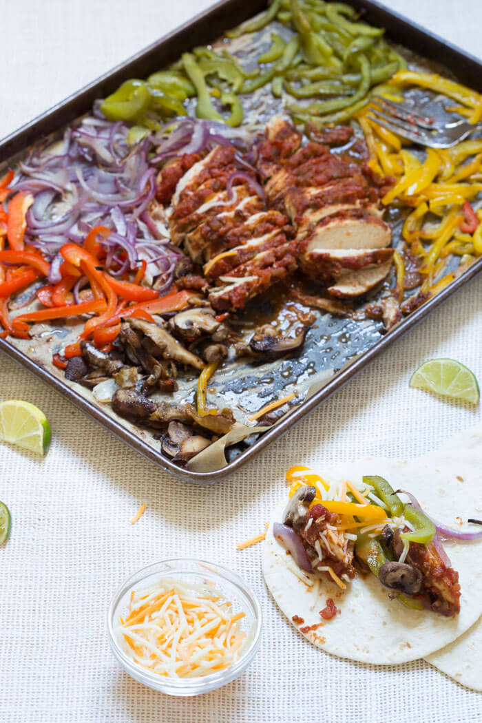 Sheet Pan Chicken Fajitas are our new weeknight dinner wonder. Check it, all the fajita veg plus super moist flavor packed chicken loaded on one pan and baked in the oven... then wrapped in soft tortillas and topped with cheddar, sour cream and avocado. What's not to love?