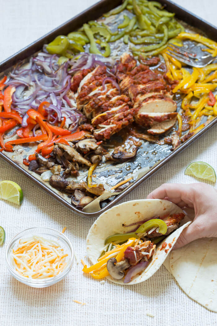 Sheet Pan Chicken Fajitas are our new weeknight dinner wonder. Check it, all the fajita veg plus super moist flavor packed chicken loaded on one pan and baked in the oven... then wrapped in soft tortillas and topped with cheddar, sour cream and avocado. What's not to love?