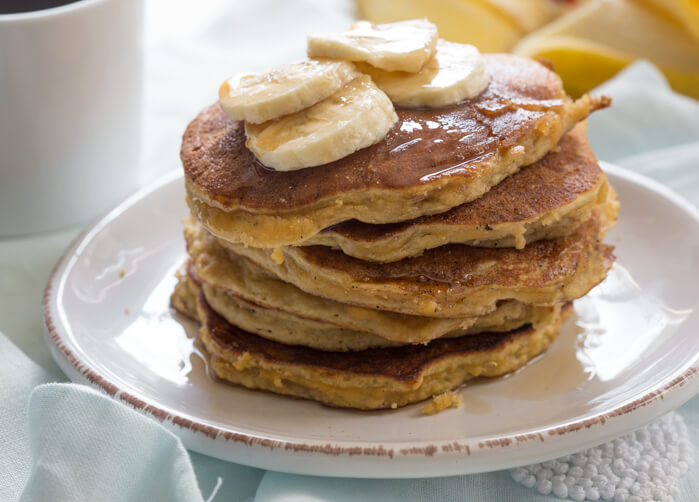 side shot of paleo banana coconut flour pancakes with sliced bananas and maple syrup