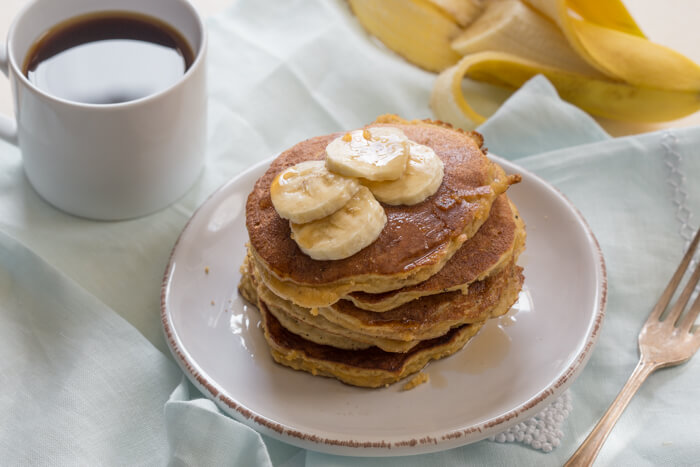 side shot of paleo banana coconut flour pancakes with sliced bananas and maple syrup