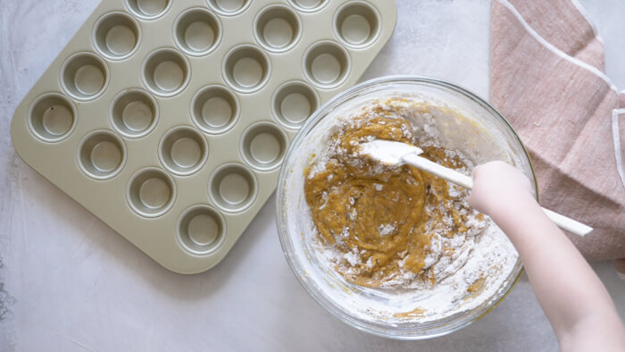 toddler helping stir pumpkin puree into muffin batter