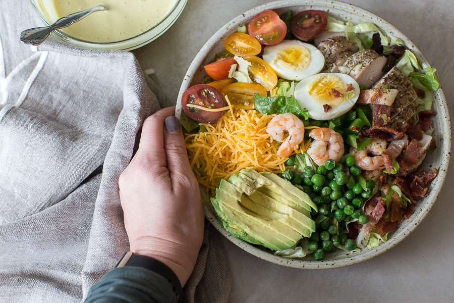 hand holding bowl of healthy cobb salad recipe and cobb salad dressing