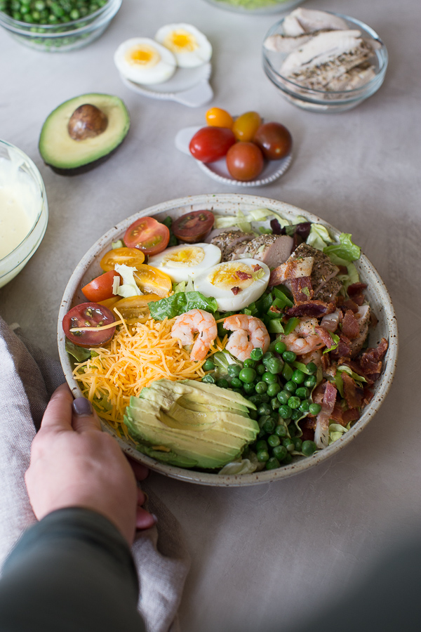 hand reaching in to grab bowl of cobb salad with shrimp and chicken