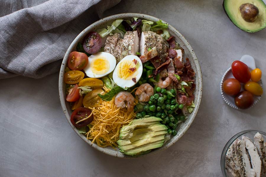 Overhead shot of healthy cobb salad recipe with eggs, bacon and avocado on an white background