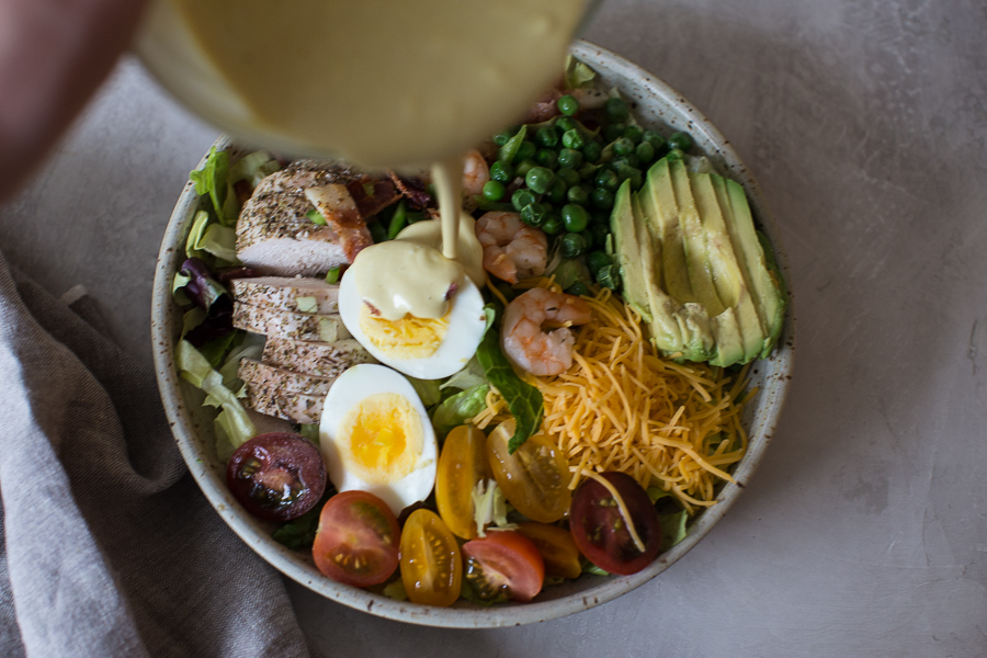 Overhead shot of healthy cobb salad recipe with eggs, bacon and avocado on an white background