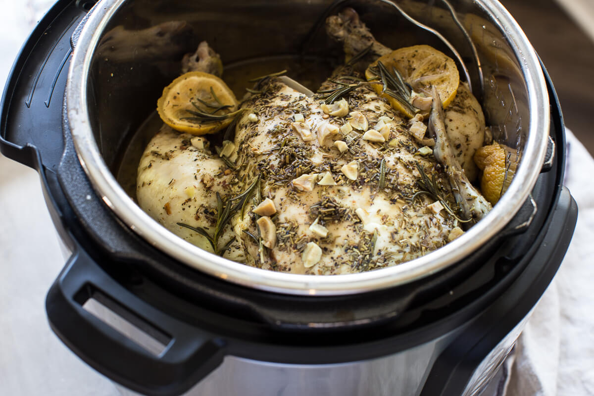 uncooked whole chicken in instant pot with lemon and fresh herbs