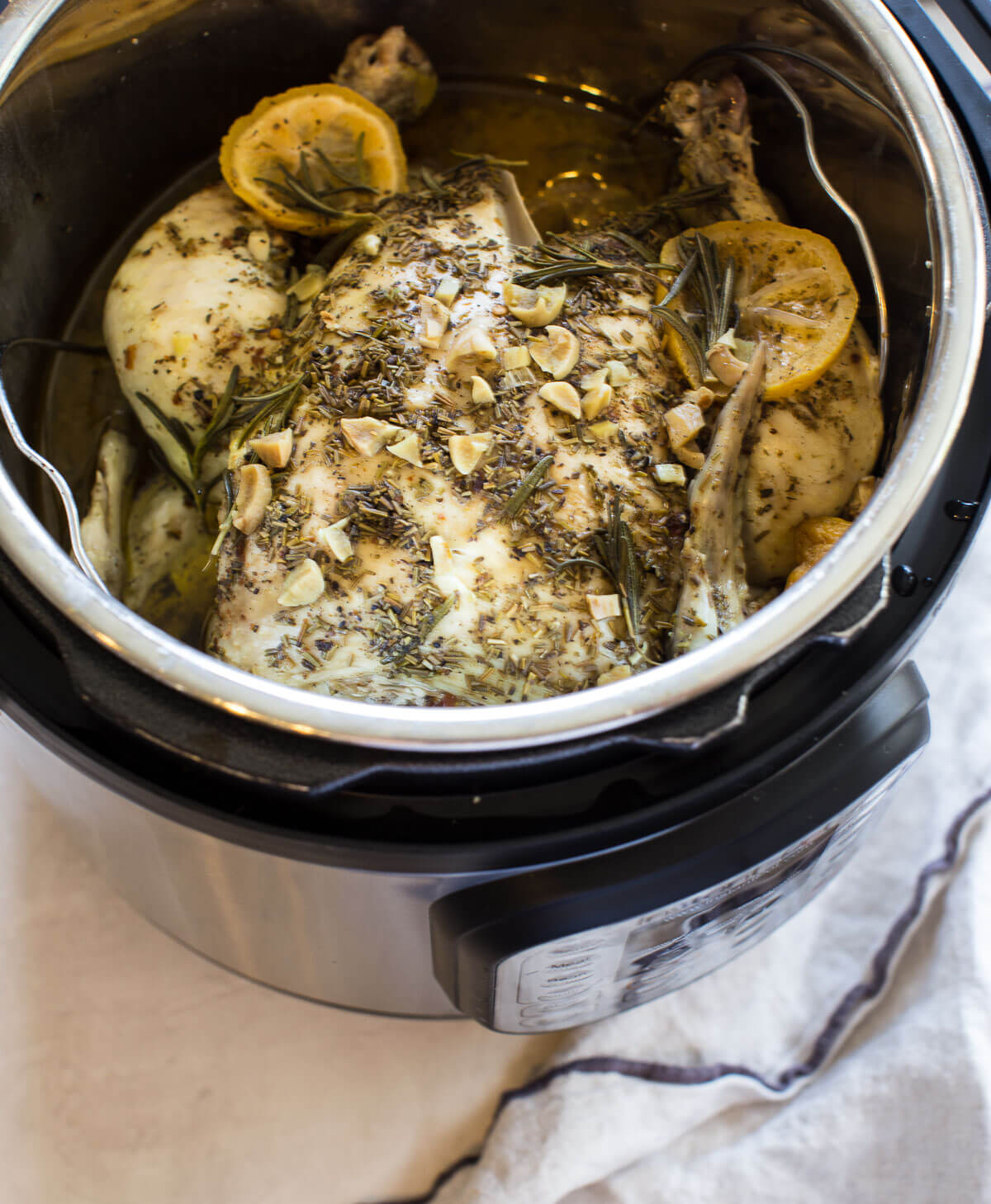 overhead shot of instant pot with whole chicken, fresh herbs, chicken broth and lemons