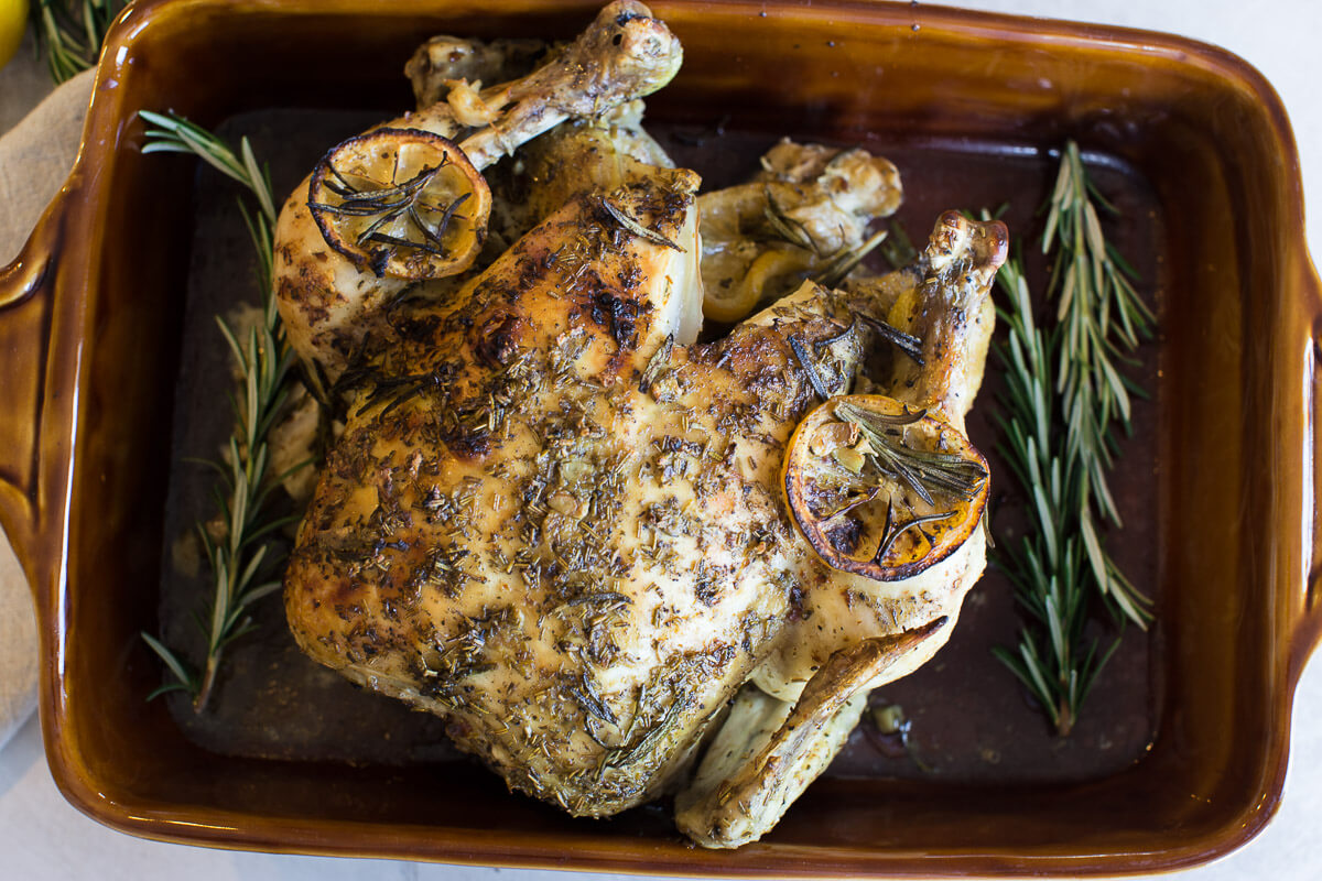 overhead shot of cooked whole chicken with fresh rosemary and lemons