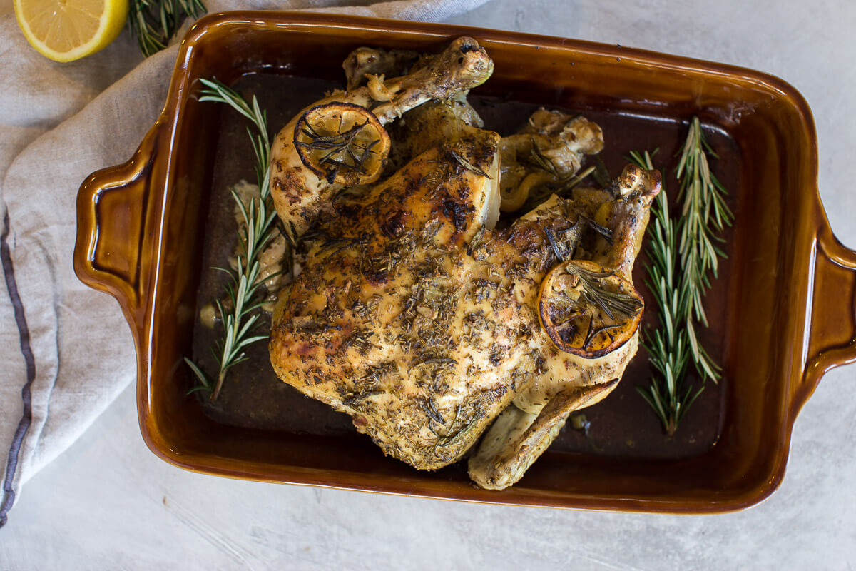 overhead shot of cooked whole chicken with fresh rosemary and lemon