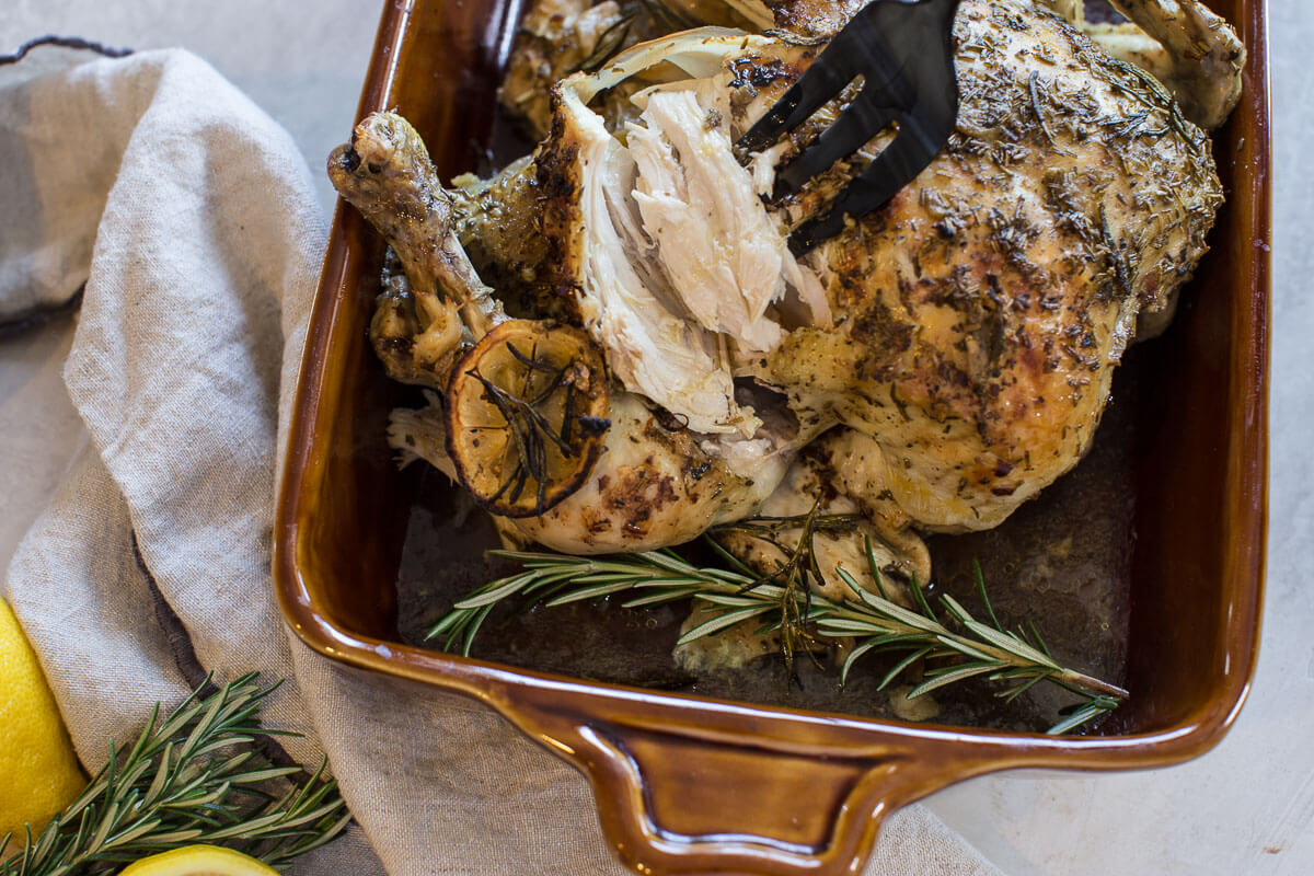 cooked whole chicken with fork pulling out white meat from center of chicken