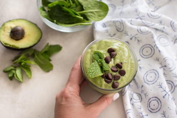 hand holding glass of creamy mint chocolate chip avocado smoothie 