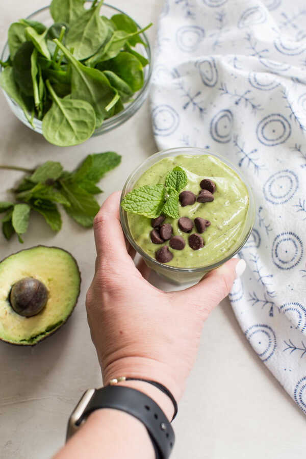 hand reaching to grab glass of mint chocolate chip avocado smoothie 