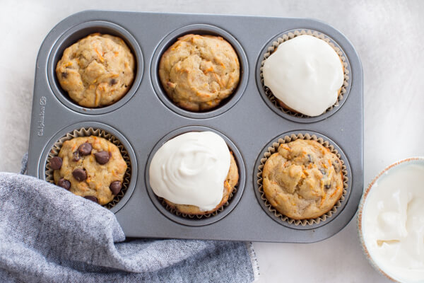 overhead shot of muffin pan with gluten free carrot cake muffins with chocolate chips, raisins, and Greek yogurt frosting