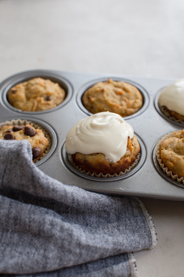 side shot of muffin pan with gluten free carrot cake muffins with chocolate chips, raisins, and Greek yogurt frosting 