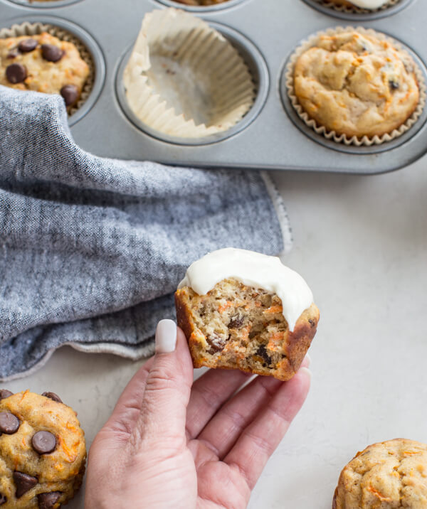 hand holding bitten gluten free carrot cake muffin with Greek yogurt frosting