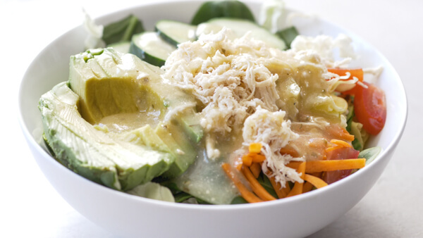 bowl of salad with shredded chicken breast, avocado, cucumbers, shredded carrots and grape tomatoes 