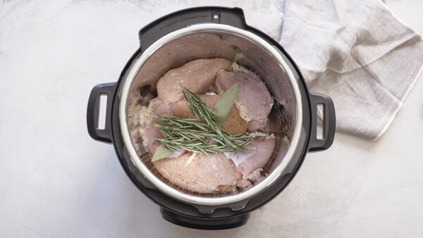 overhead shot of frozen chicken breast in Instant Pot with fresh herbs
