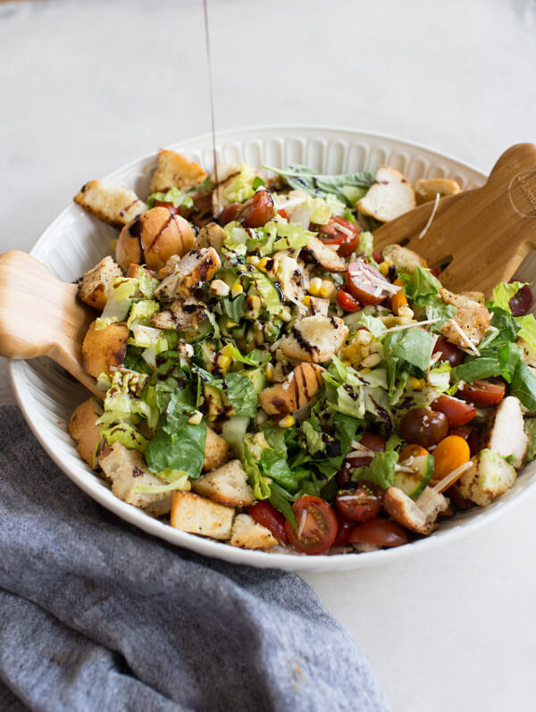 "End of Summer" Chicken Panzanella Salad recipe made with fresh tomatoes, cucumbers, homemade croutons, grilled corn, fresh basil, avocado, parmesan cheese. It's packed with perfectly seasoned grilled chicken for satiating protein and smothered in a thick balsamic vinegar. YUM!