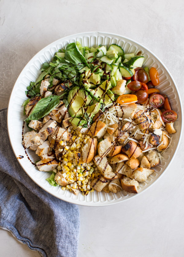 "End of Summer" Chicken Panzanella Salad recipe made with fresh tomatoes, cucumbers, chunks of toasty garlic bread, grilled corn, fresh basil, parmesan cheese. It's packed with perfectly seasoned grilled chicken for satiating protein and smothered in a thick balsamic vinegar. YUM!